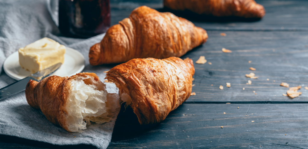 Croissant torn in half, sitting on a wooden table with butter and a butter knife beside it.