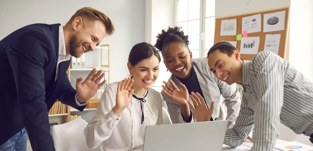 Four people waving at a laptop screen.