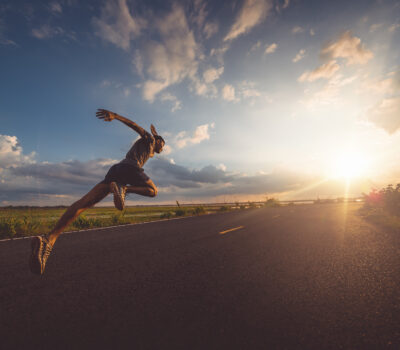 Man outdoors running down a road towards the sun