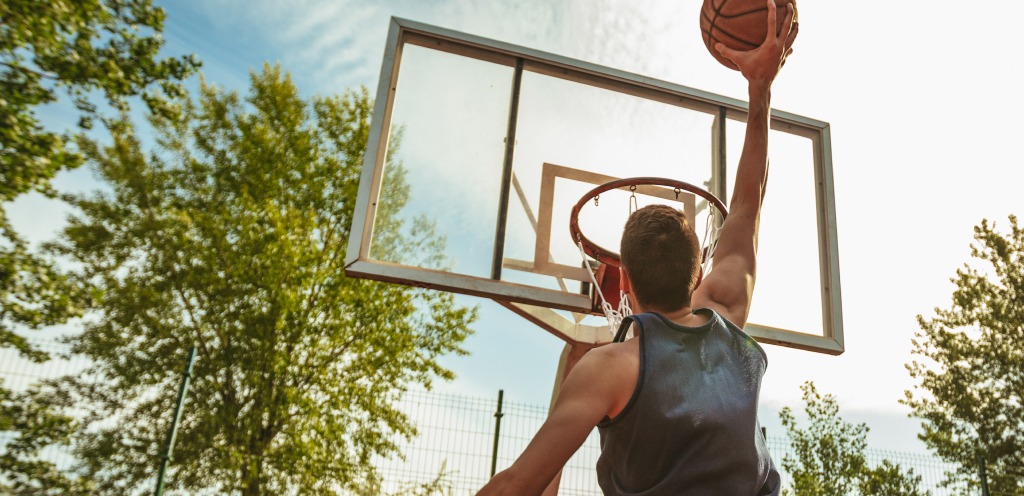 View from behind of a man dunking a basketball with trees and a blue sky in the background.