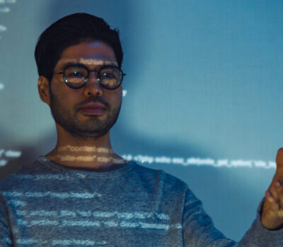 Indian man standing in front of a screen with computer code projected over top of him.