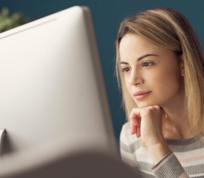 Young attractive woman sitting at desk and working with her computer, she is smiling and looking at the screen