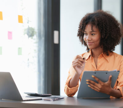 Woman working on laptop consulting a checklist