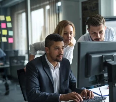 Man in suit working on his laptop with team members looking on.